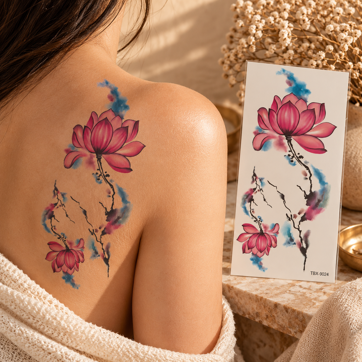 Pink lotus watercolor temporary tattoo designs with black branches and blue-purple accents shown on a shoulder and sheet