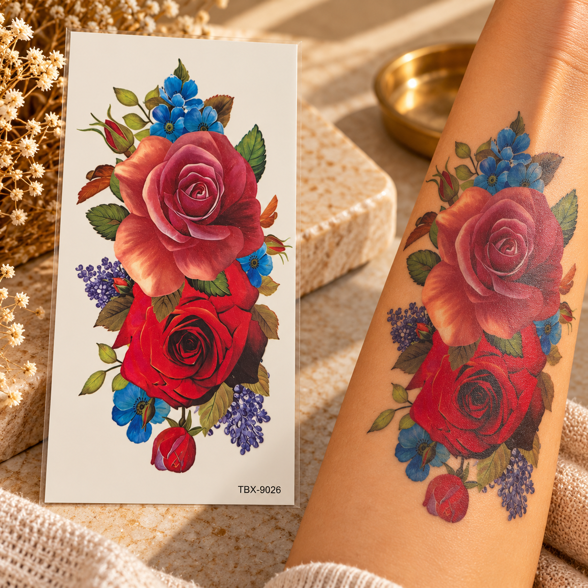 Red and pink rose bouquet temporary tattoo with blue and purple floral accents shown on a sheet and applied to an arm