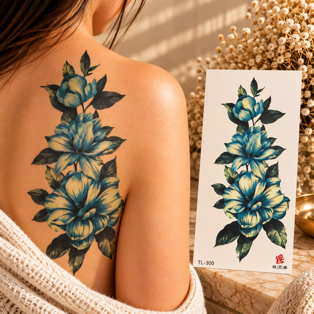 Blue and golden-yellow floral statement temporary tattoo with dark green foliage shown on a shoulder beside the sheet