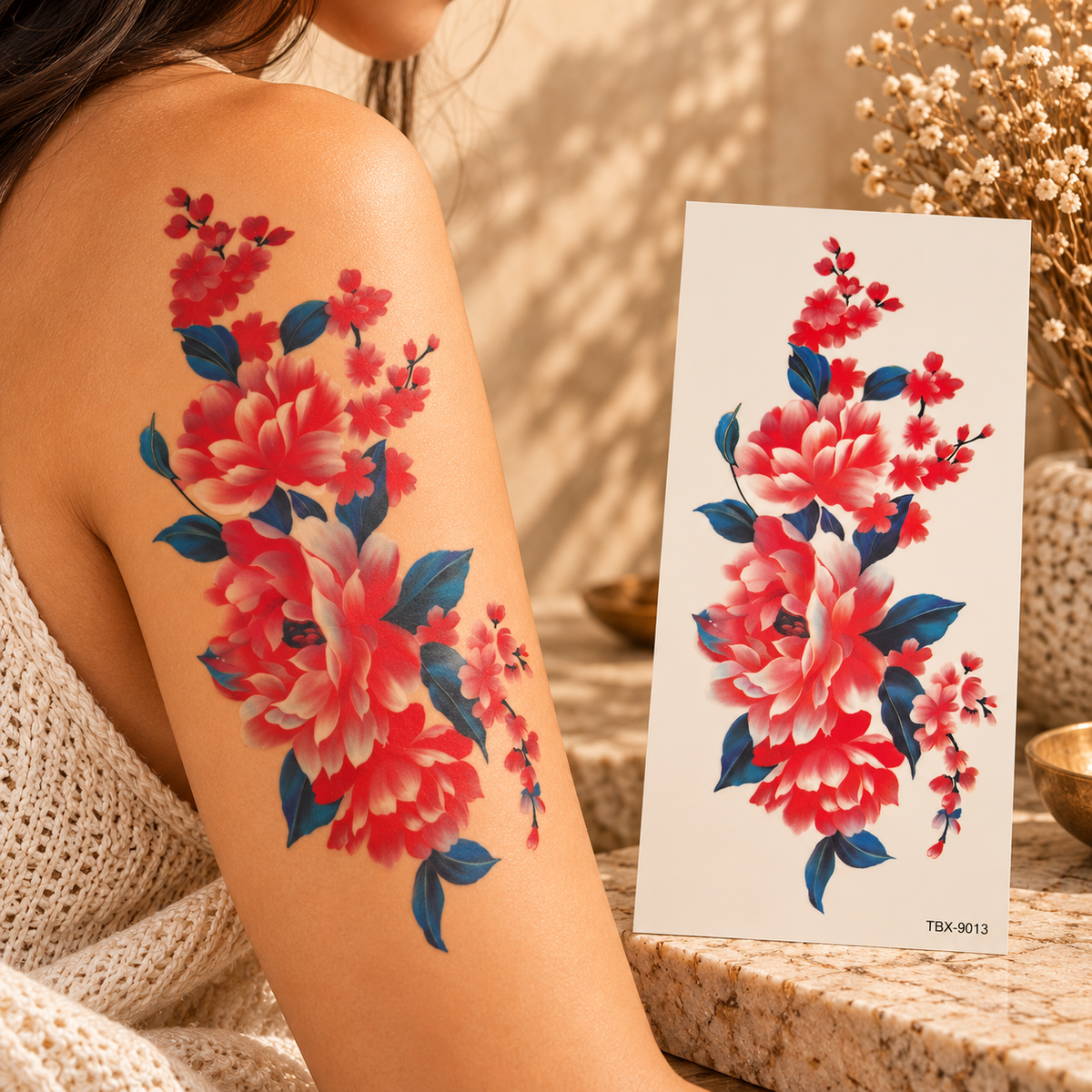 Red and coral floral temporary tattoo with deep-blue leaves shown on an upper arm beside the tattoo sheet