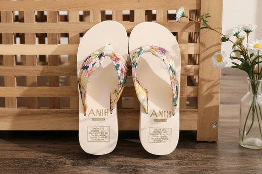 Pair of beige flip-flops with floral straps on a wooden surface.