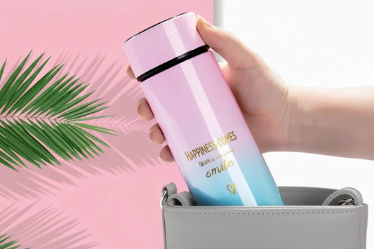Gradient pink to blue thermos with motivational quote held by a hand against a pink background with green leaves.